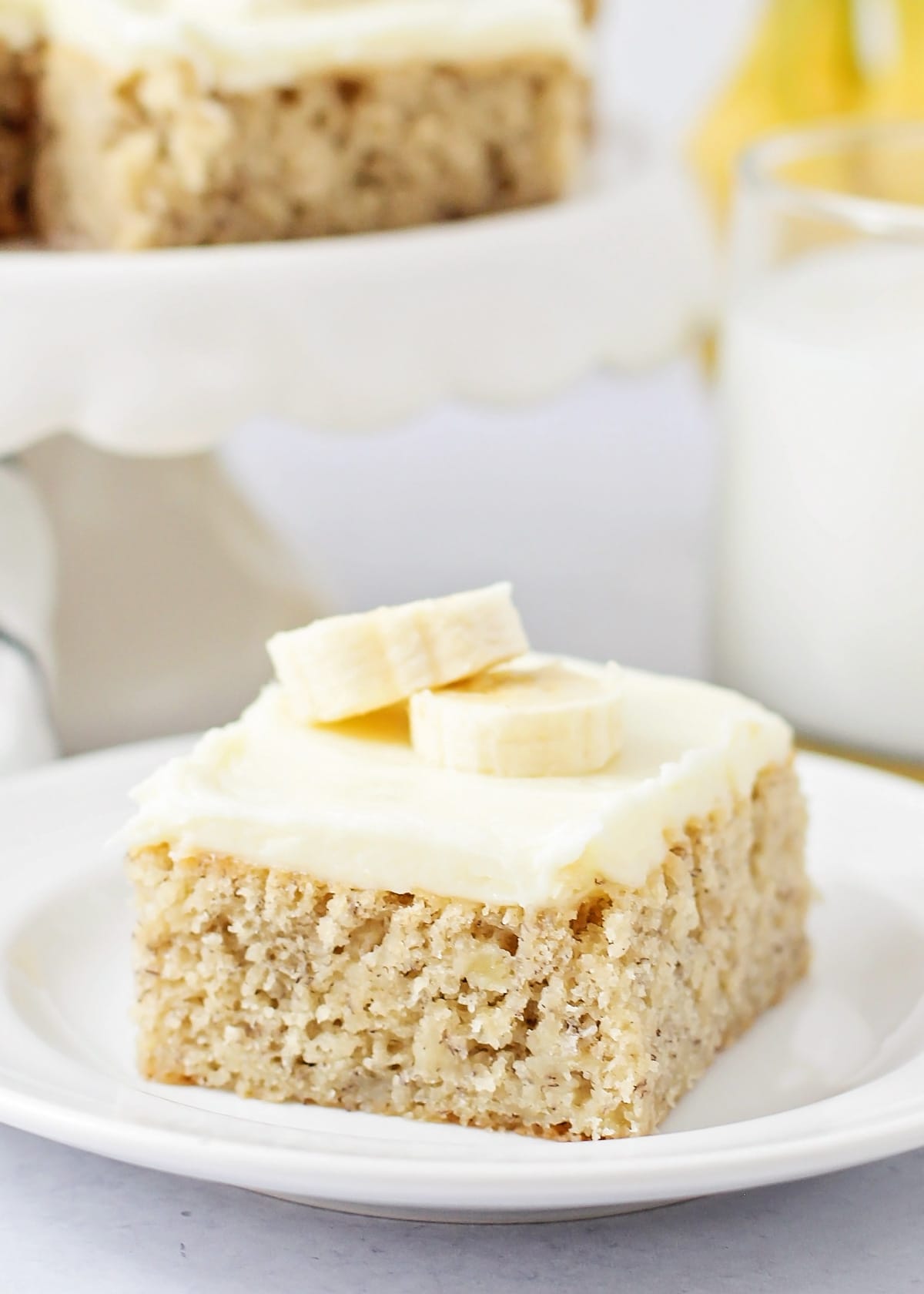 Banana bars slice topped with cream cheese frosting and sliced banana.