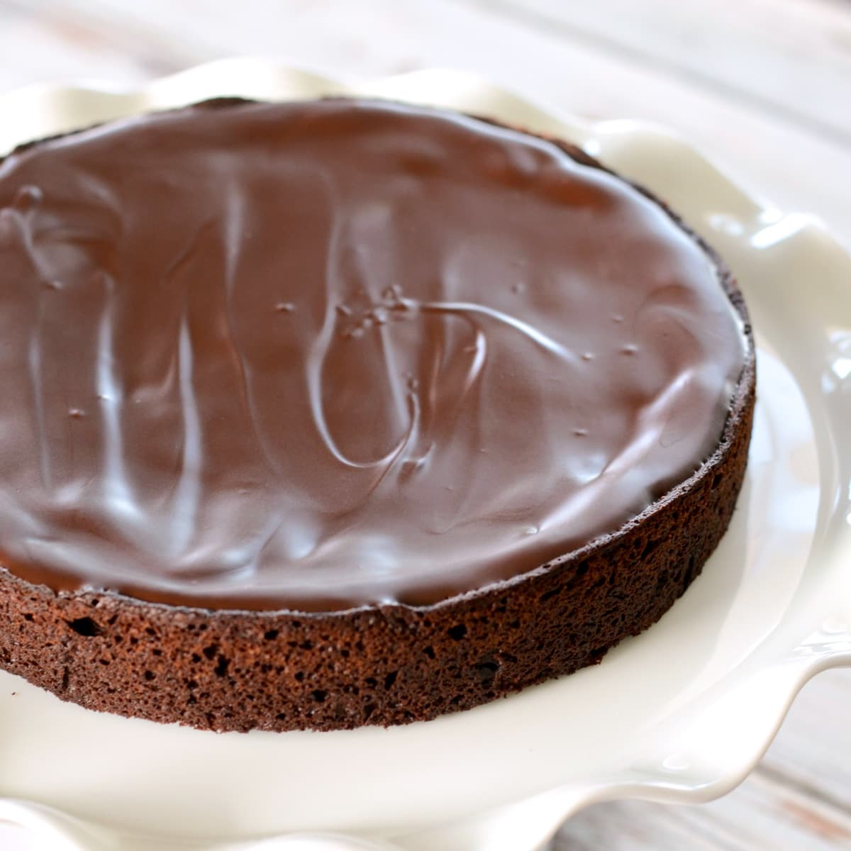 Chocolate cake topped with chocolate icing on a white plate.