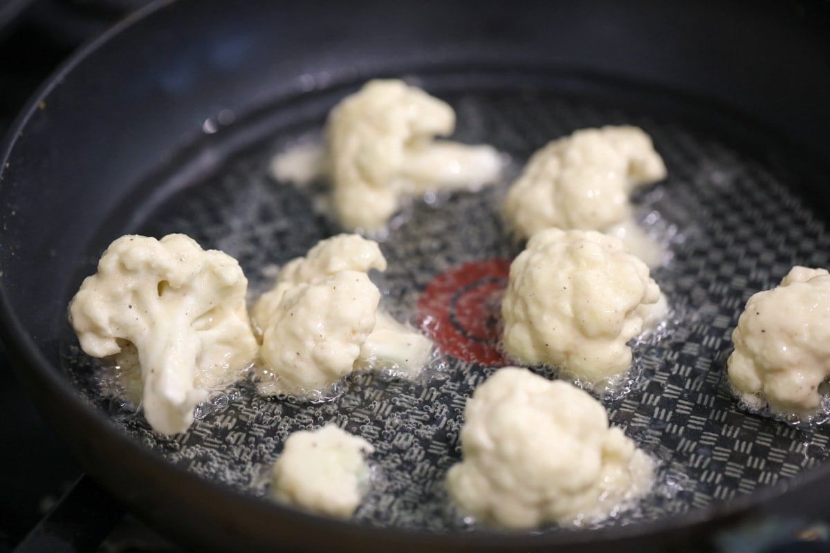 Fried cauliflower cooking in a pan of oil.