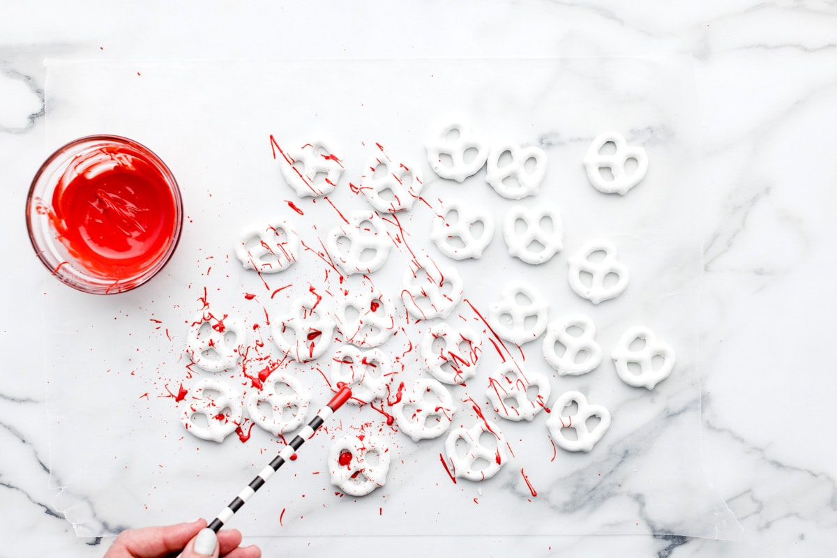 Spraying candy blood on halloween pretzels with a straw.