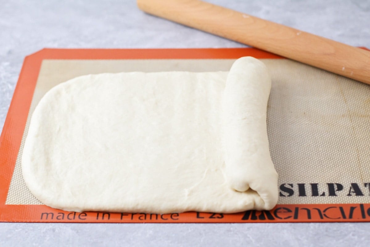 Bread dough rolled out and being rolled up.