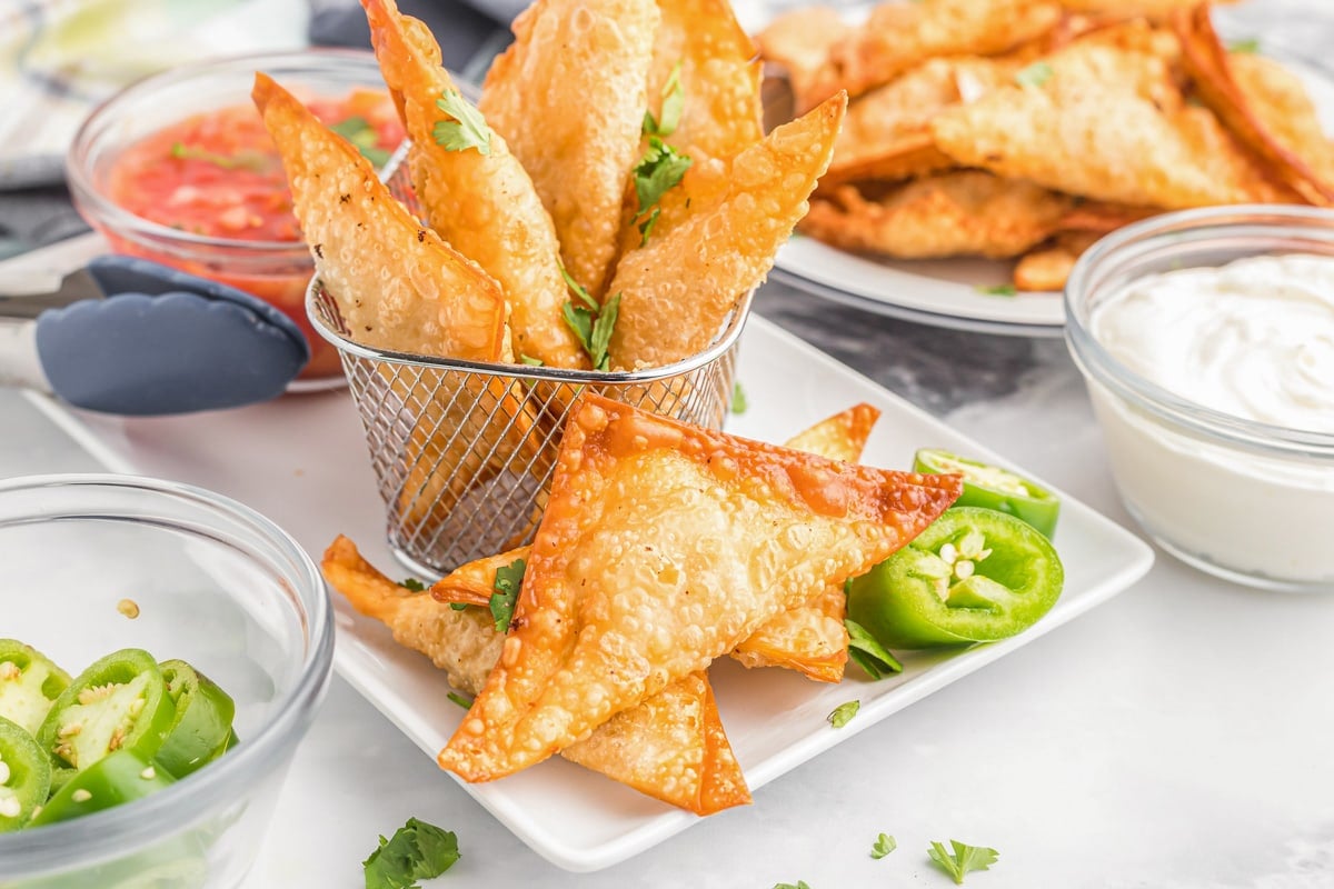 Easy Appetizers - Mexican Wontons on a white plate garnished with jalapeno peppers and served with a side of red salsa. 