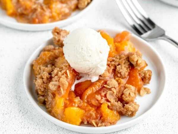 A serving of easy peach crisp recipe topped with a scoop of vanilla ice cream.