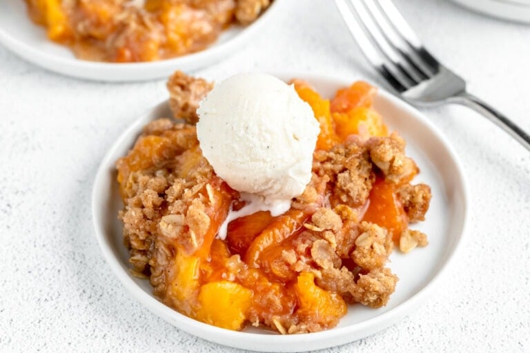 A serving of easy peach crisp recipe topped with a scoop of vanilla ice cream.