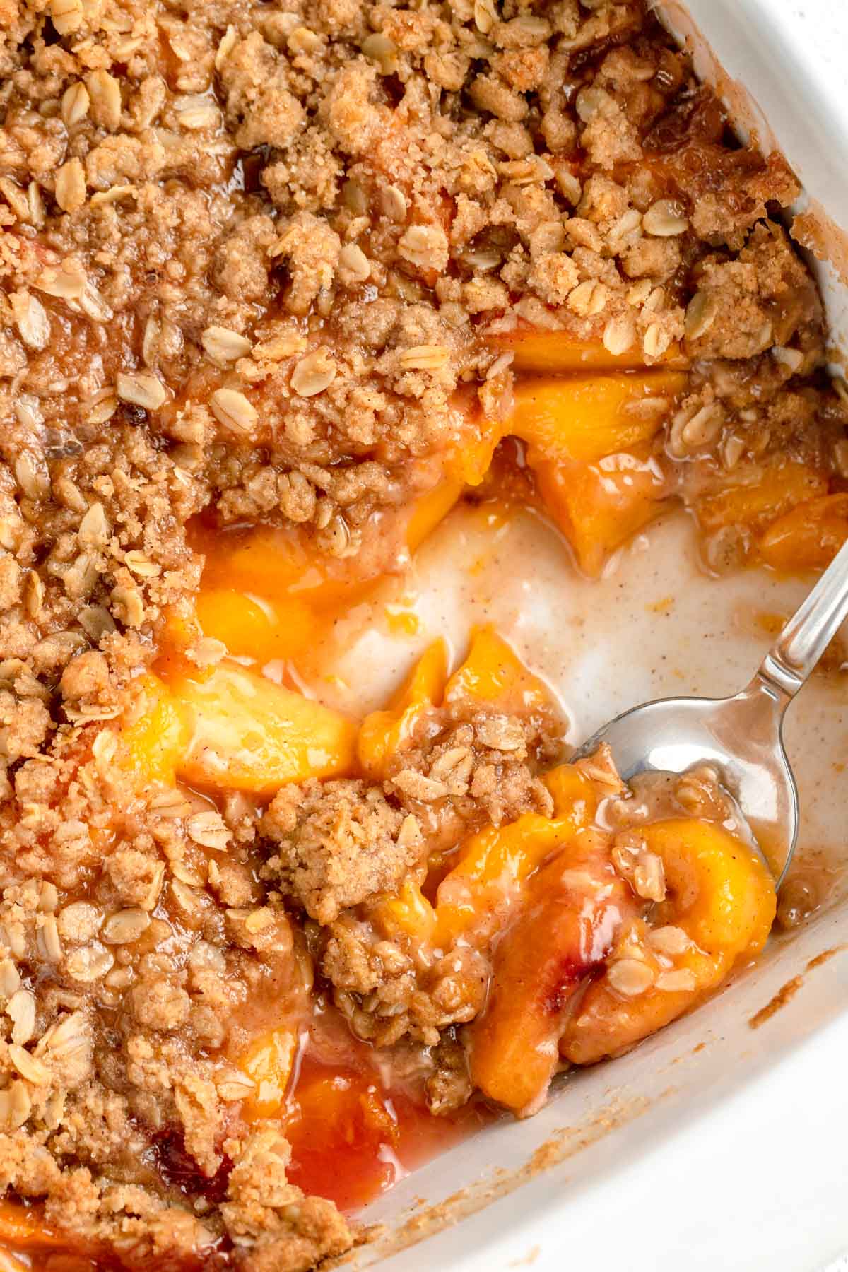 Close up image of homemade classic peach crisp recipe with a scoop mixing.