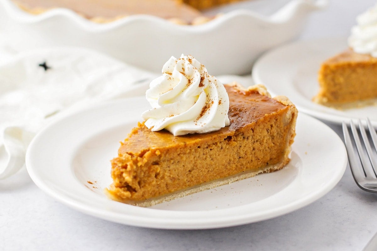 Pumpkin Pie on a white plate topped with whipped cream.