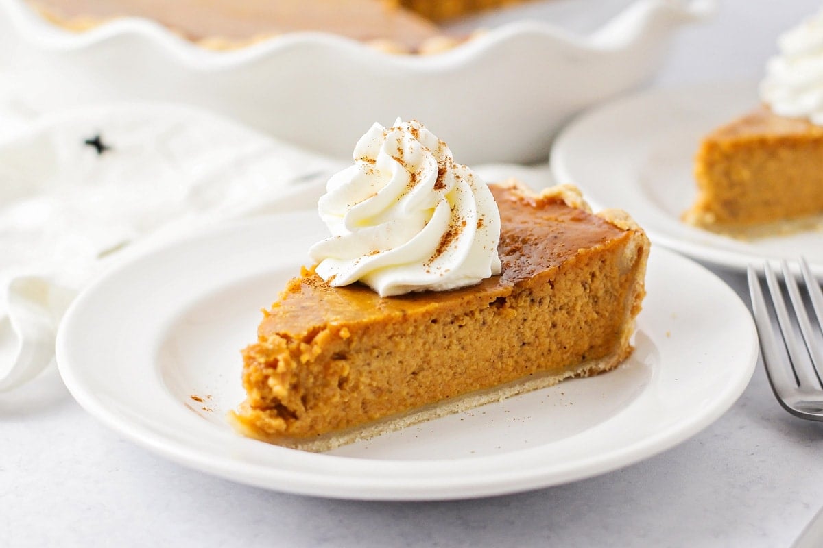 A slice of pumpkin pie topped with whipped cream on a white plate.