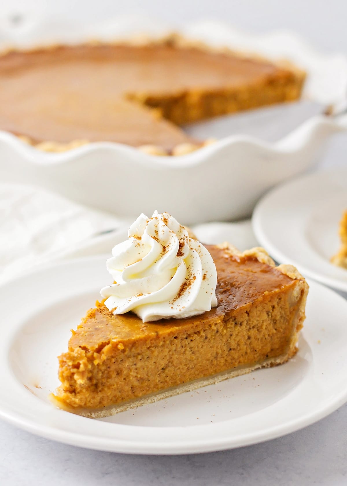 Slice of homemade Pumpkin Pie Recipe on a plate topped with whipped cream.