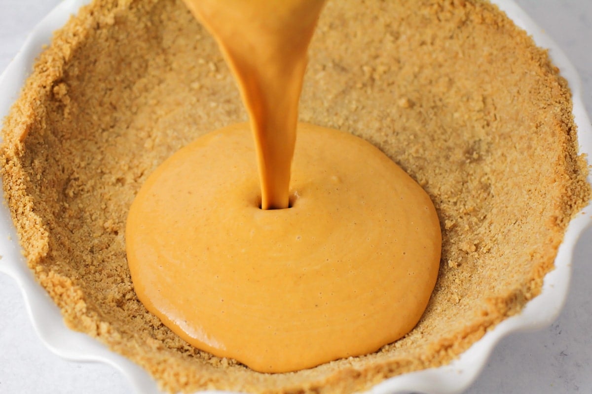 Pouring the pumpkin pie filling into the graham cracker crust.