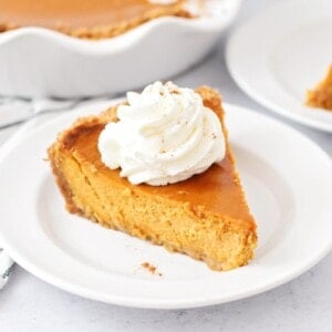 A slice of pumpkin pie with graham cracker crust topped with whipped cream.
