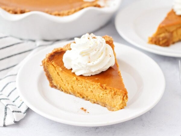 A slice of pumpkin pie with graham cracker crust topped with whipped cream.