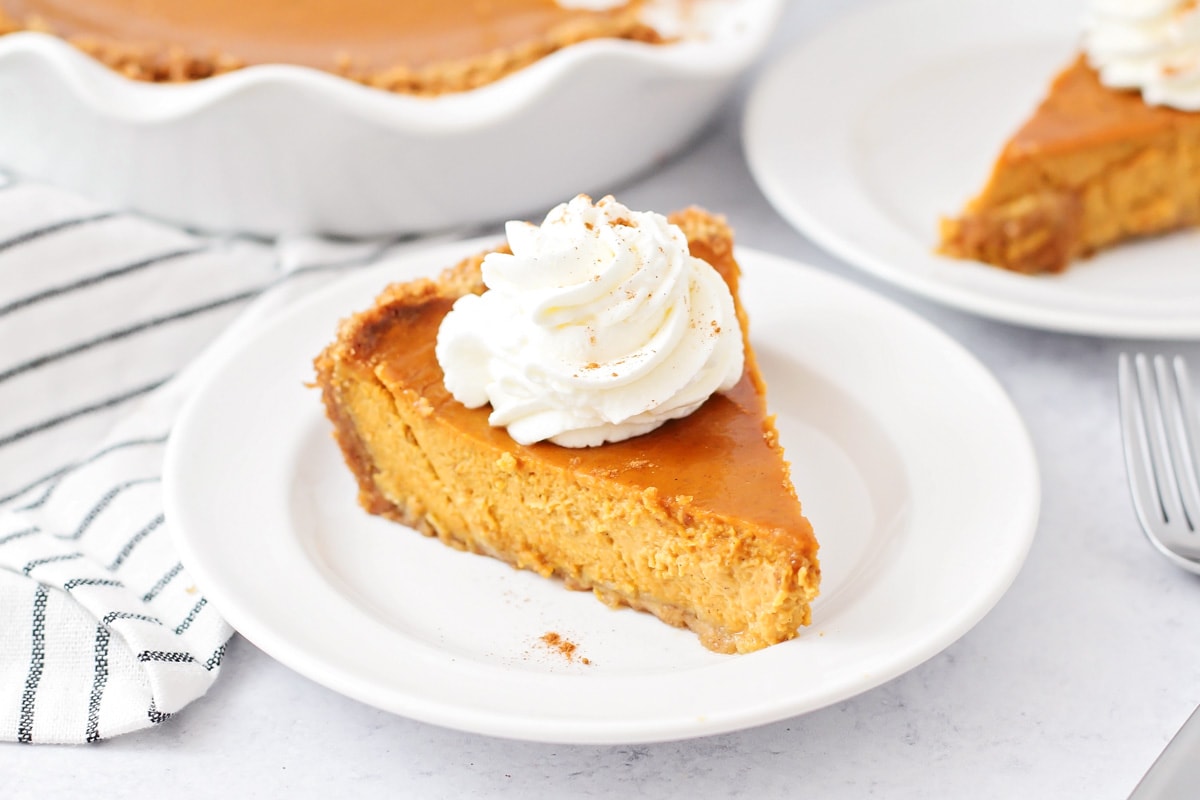 A slice of pumpkin pie with graham cracker crust topped with whipped cream.