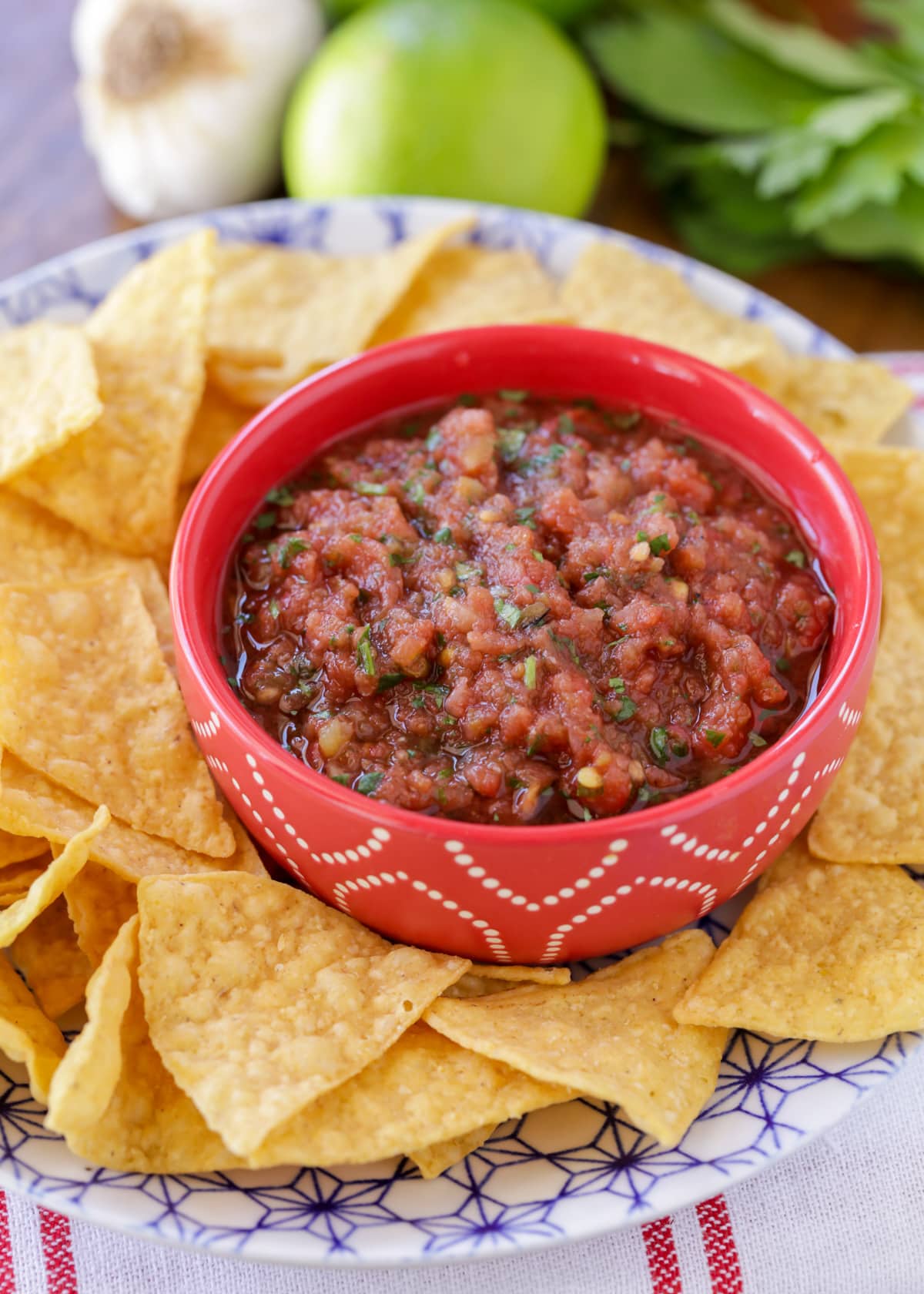 Easy homemade salsa recipe in small bowl on plate with tortilla chips.