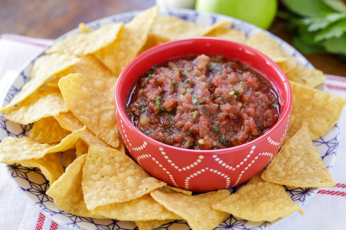 Our favorite homemade salsa recipe in a small, red bowl with tortilla chips.