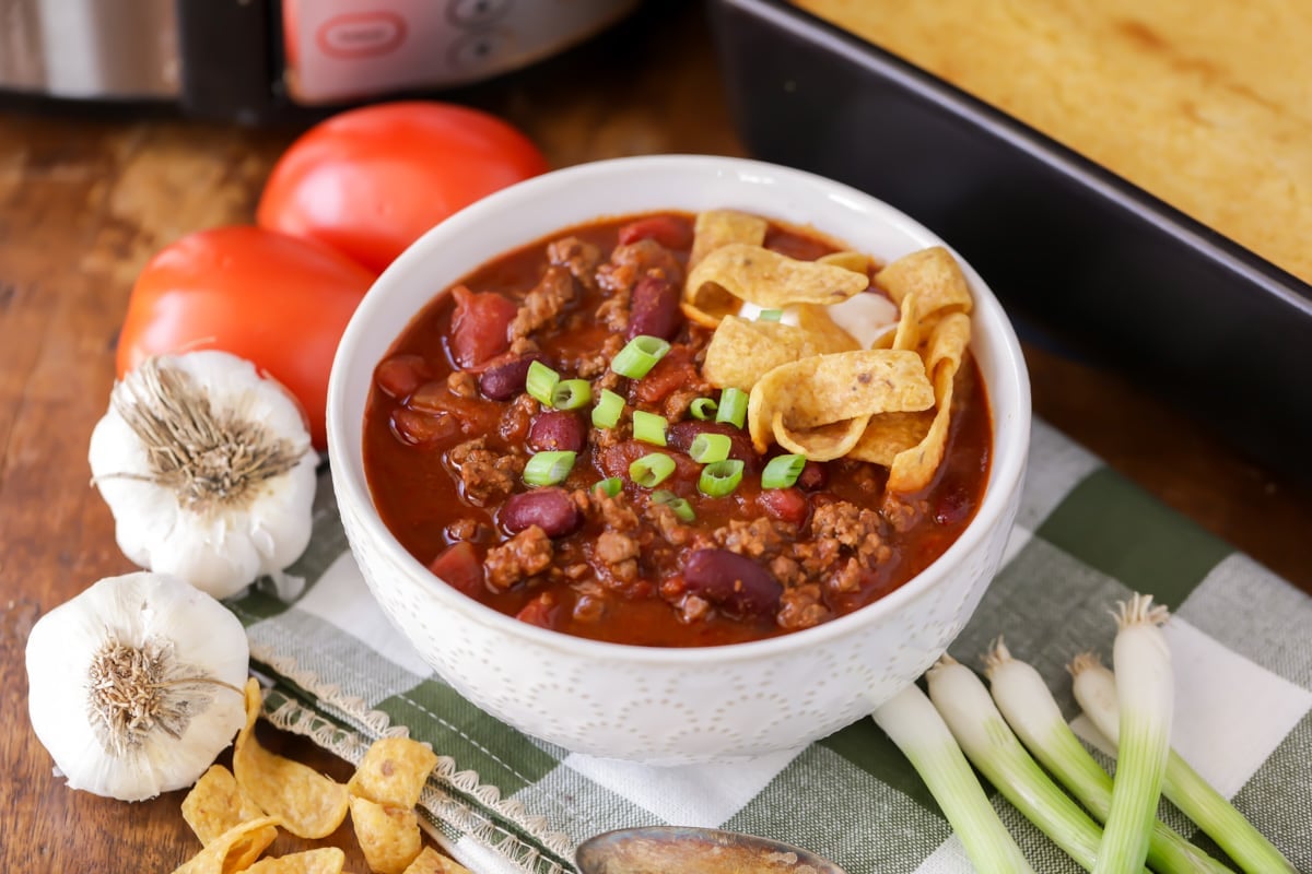 A white bowl of slow cooker chili topped with green onions and fritos.