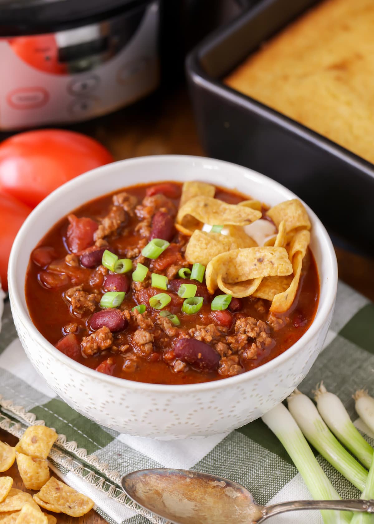 A bowl of slow cooker chili topped with green onions and fritos.
