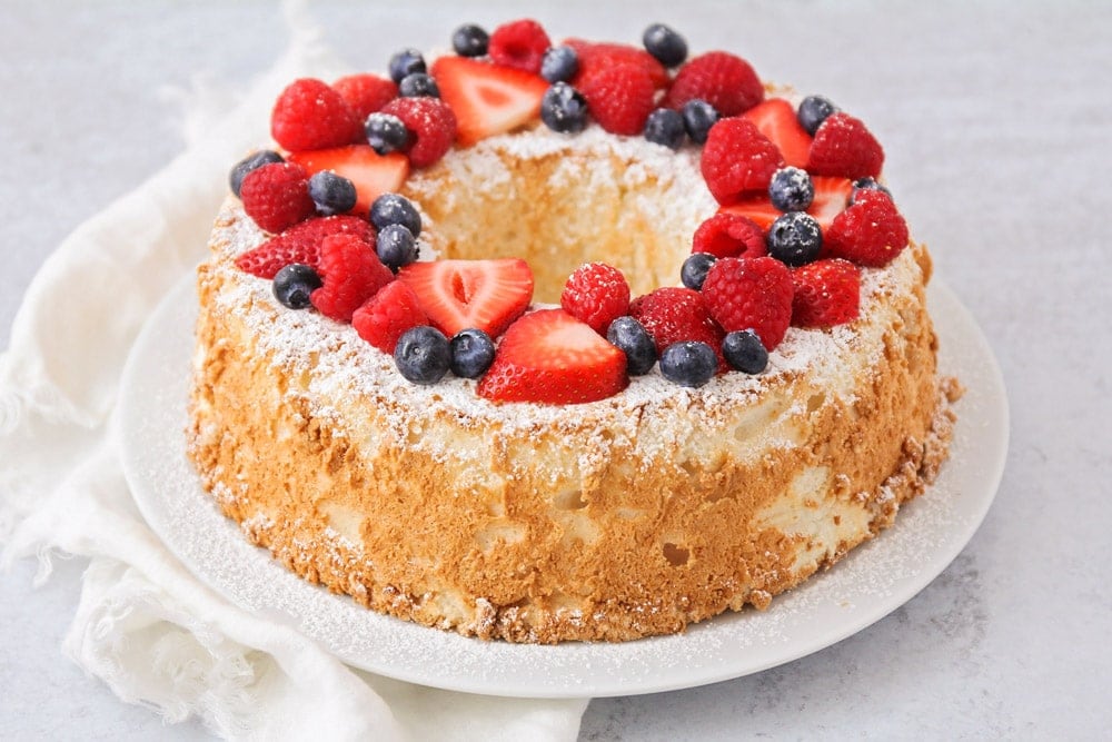 Valentine's Day Desserts - Angel Food Cake topped with a dusting of powdered sugar, strawberries, raspberries and blueberries on a white plate. 