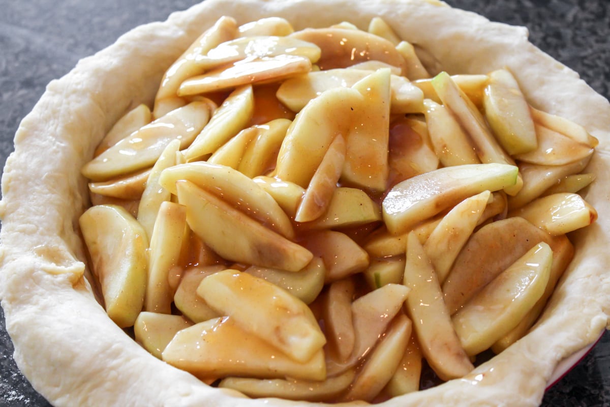 Apple pie filling poured into homemade pie crust in dish.