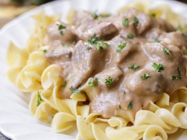 Easy beef stroganoff recipe on egg noodles on white plate.