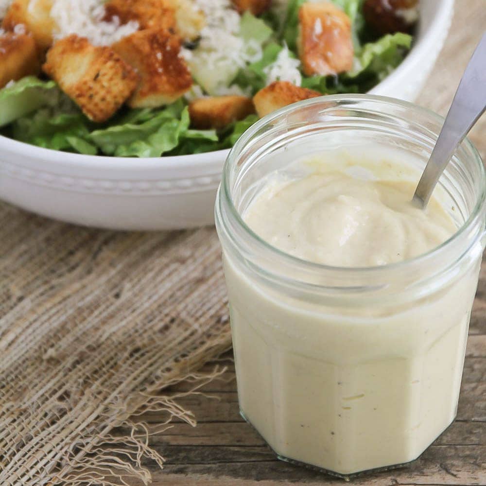 Homemade Caesar dressing in a glass jar with a metal spoon.
