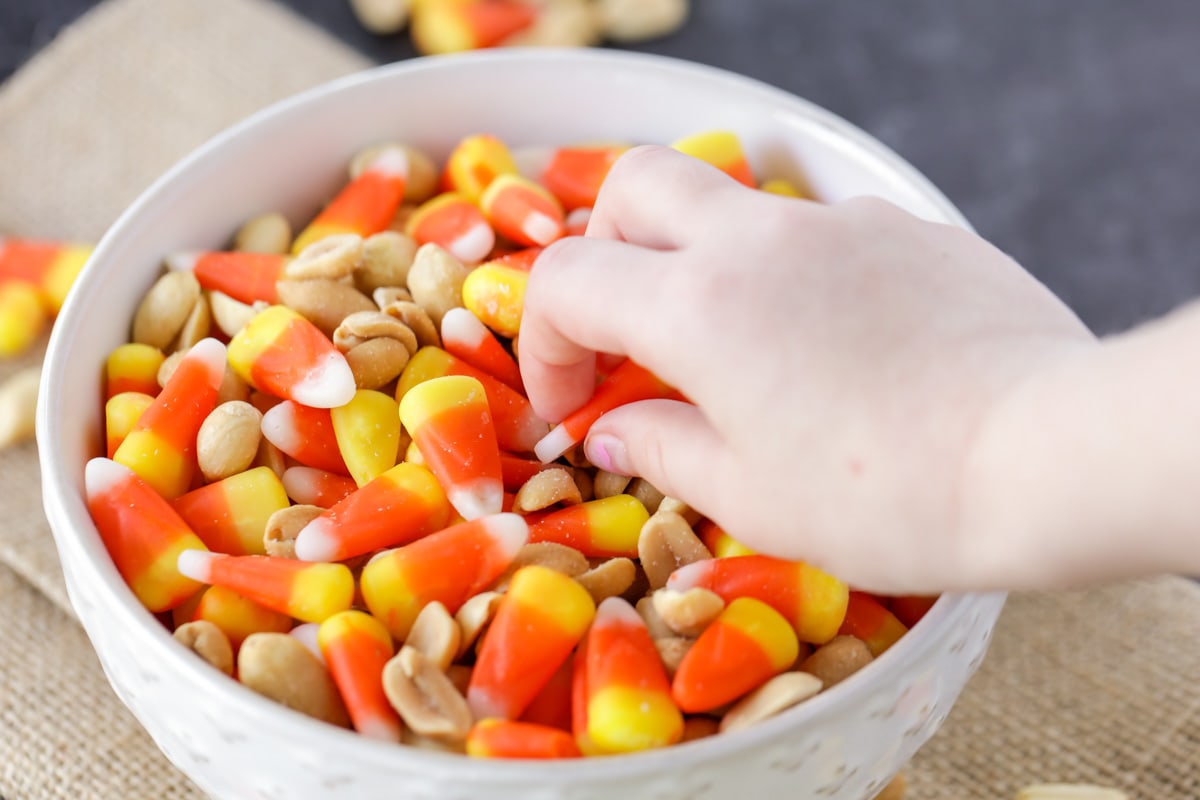Little hand grabbing candy corn peanut mix from bowl.