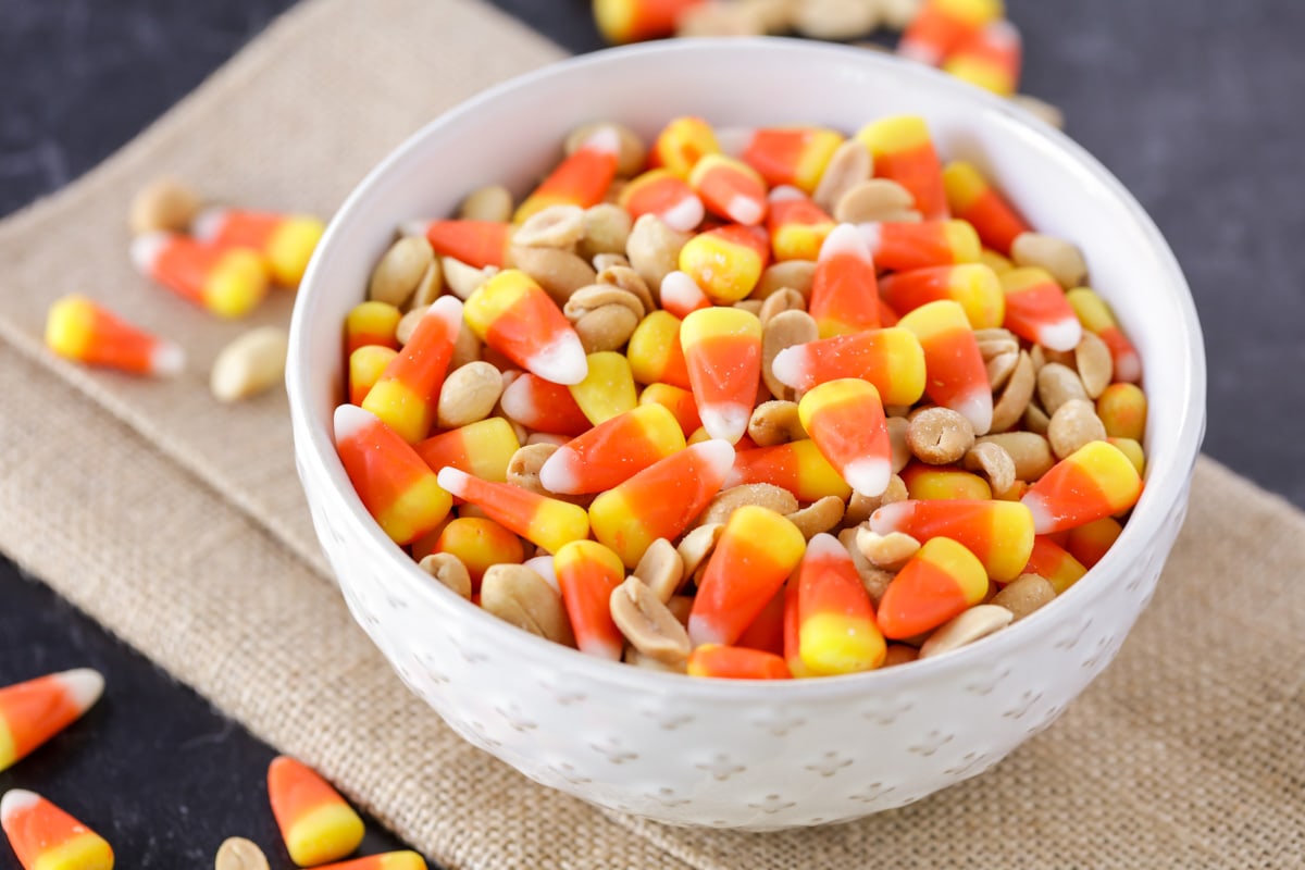 Candy corn and peanuts mix in white bowl.