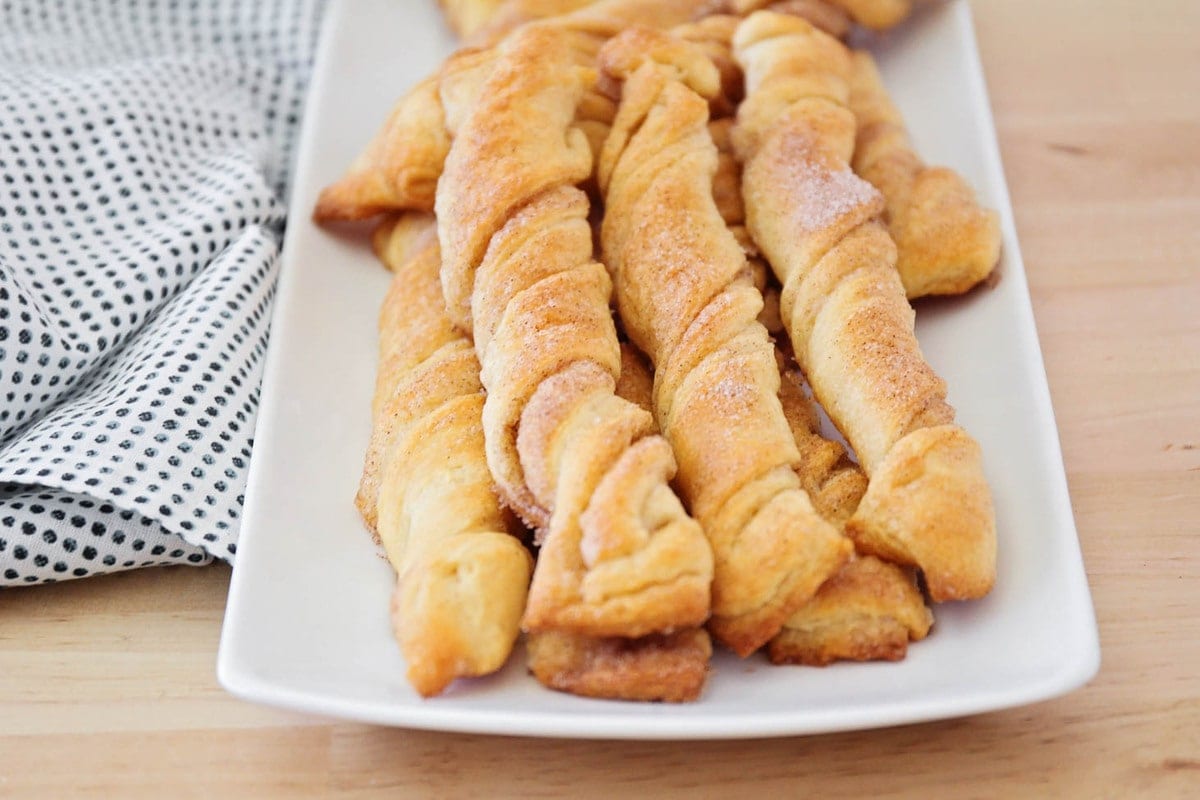 Flaky cinnamon twists are buttery and sweet. They take only 15 min. to make, and will disappear in minutes!! A pile of cinnamon twists on a serving tray.