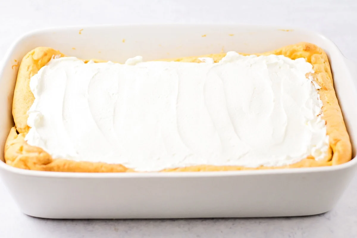 Whipped cream spread on top of a baked cream puff cake with pudding.