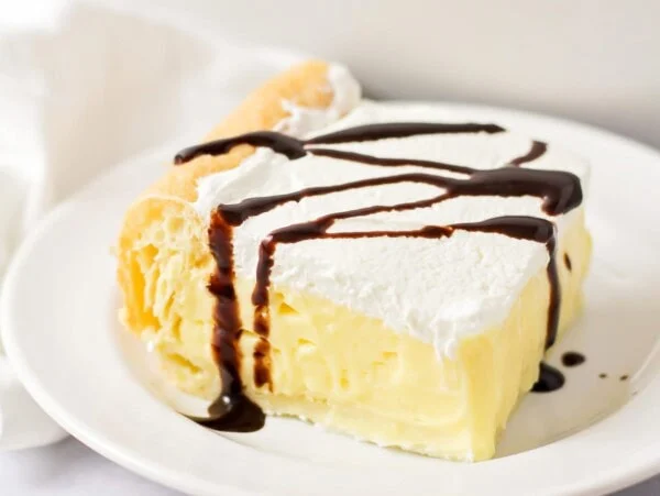 A slice of cream puff cake drizzle with chocolate sauce.