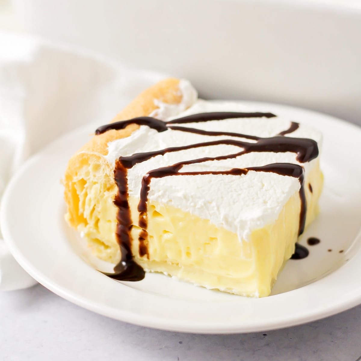 A slice of cream puff cake drizzled in chocolate sauce.