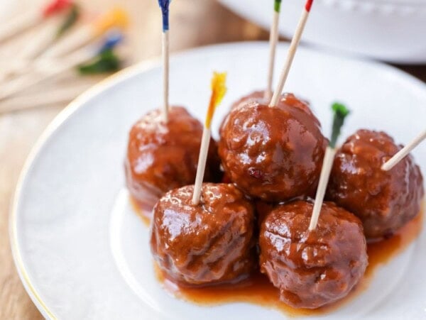 Crock pot meatballs with toothpicks in them on white plate.