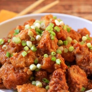 Crockpot orange chicken topped with green onions served in a white bowl.