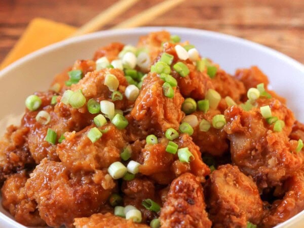 Crockpot orange chicken topped with green onions served in a white bowl.