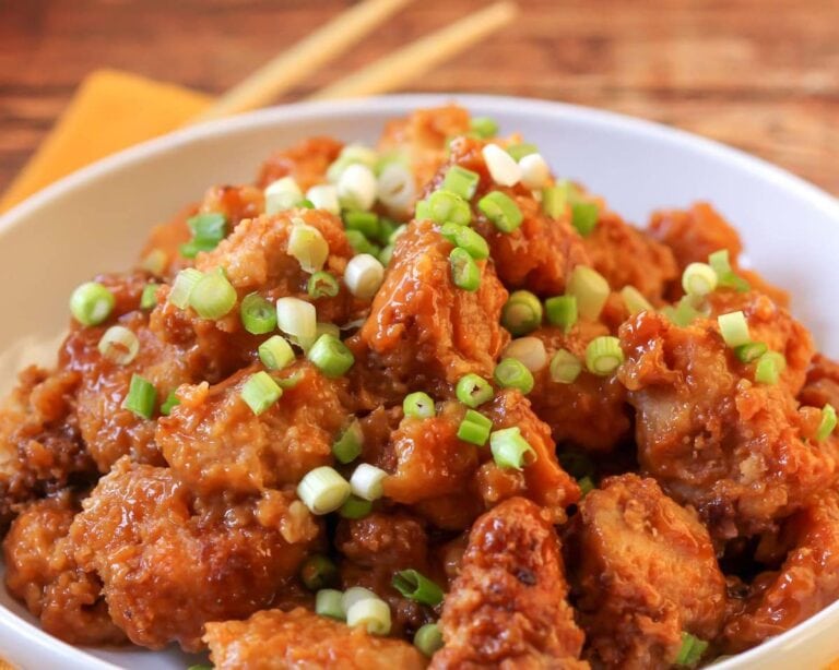 Crockpot orange chicken topped with green onions served in a white bowl.
