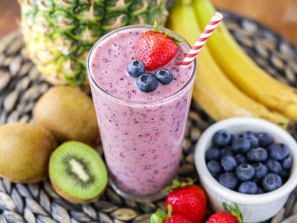 A blend fresh fruit smoothie in a glass surrounded by fruit.