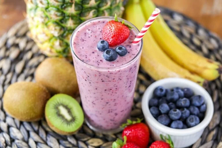 A blend fresh fruit smoothie in a glass surrounded by fruit.