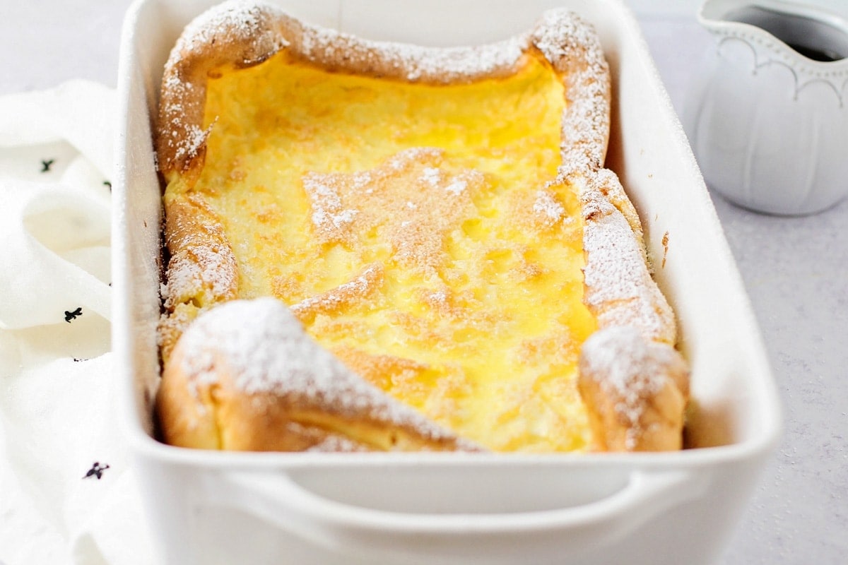 A german pancake topped with powdered sugar in a white baking dish.