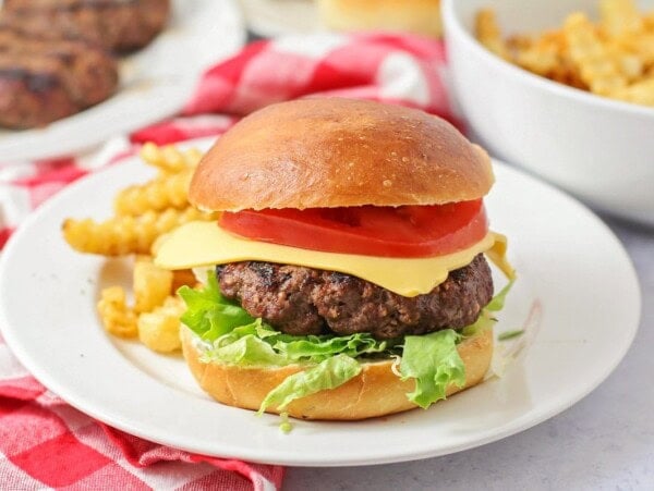Best burger recipe with all the toppings on a white plate with French fries.