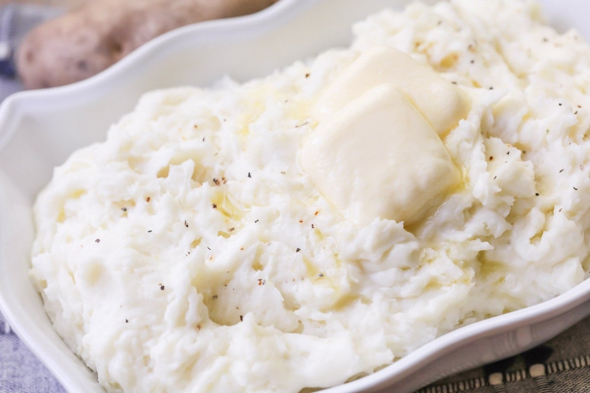 A white casserole dish of best mashed potatoes topped with butter pats.