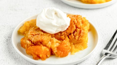 A serving of peach dump cake topped with whipped cream.