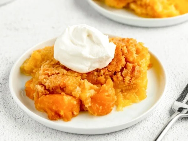 A serving of peach dump cake topped with whipped cream.