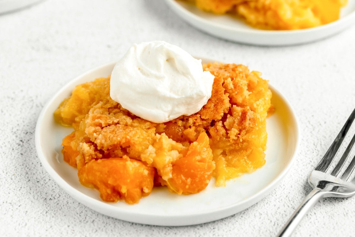Peach dump cake with whipped cream on top on plate.