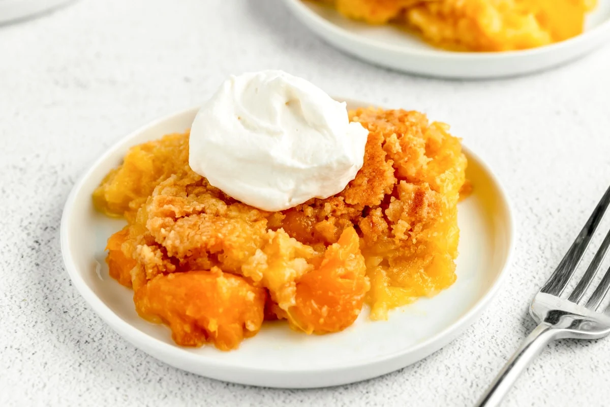 Peach dump cake with whipped cream on top on plate.