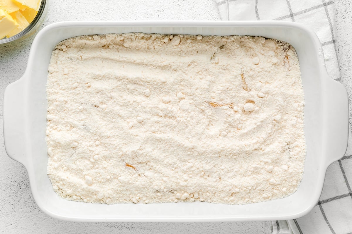 Cake mix poured over peach slices in baking dish.