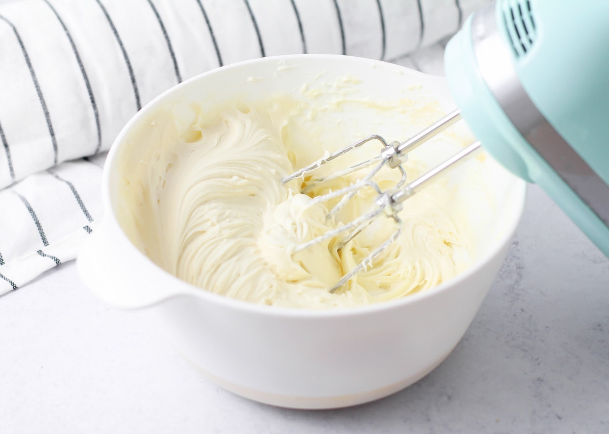 A mixing bowl filled with cream cheese frosting for filling pumpkin roll.