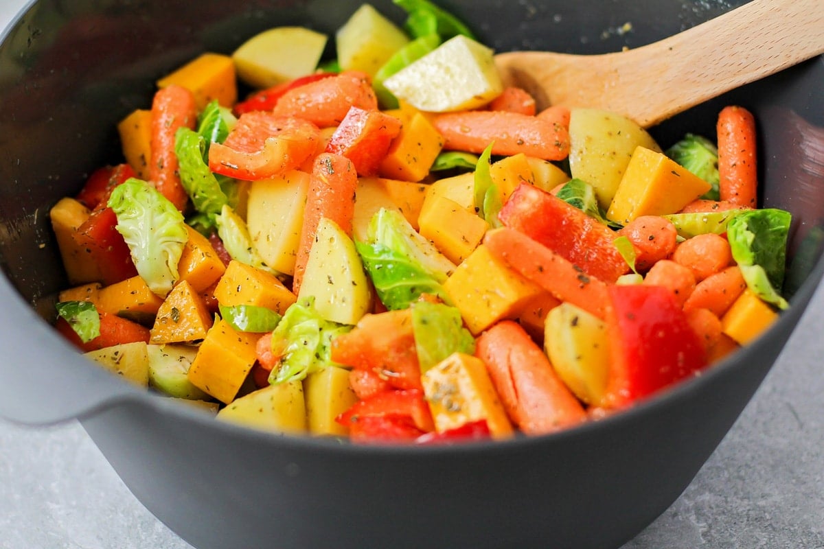 A variety of vegetables with seasonings on them in a mixing bowl.