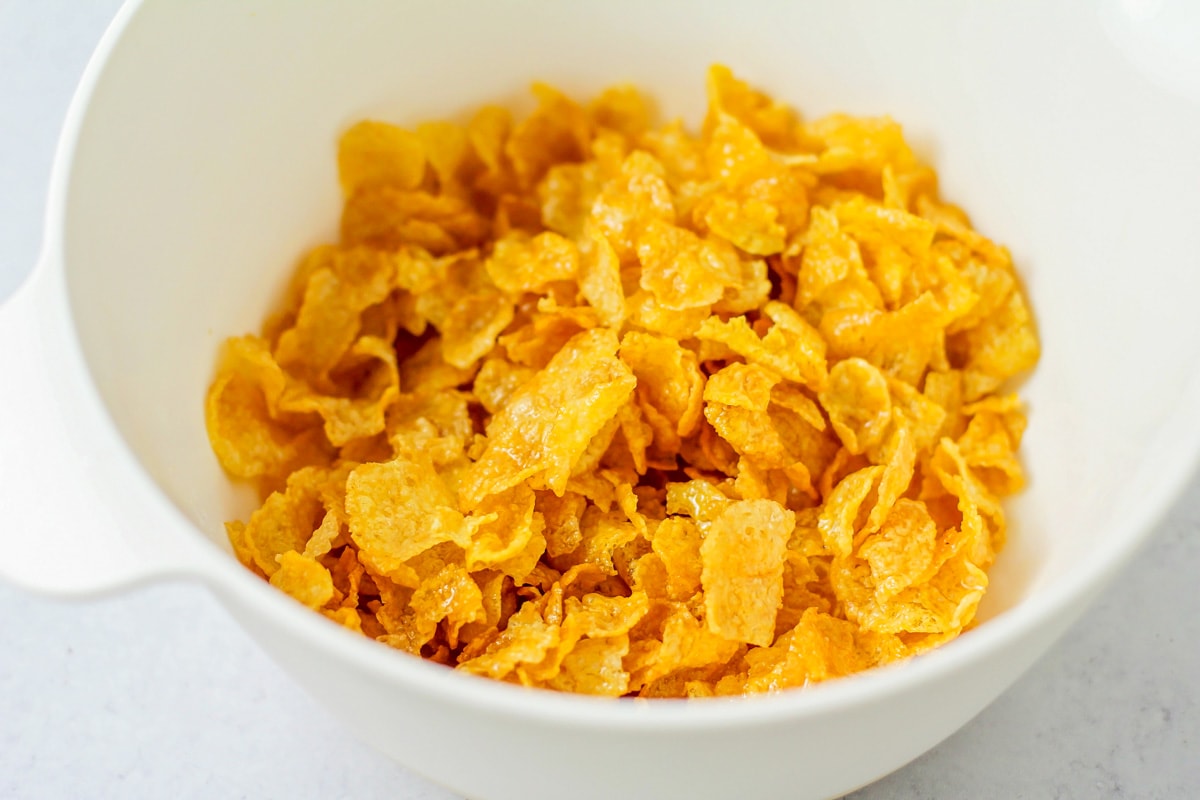 Cornflakes for topping crockpot hashbrown casserole in a bowl.