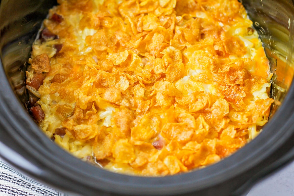 Cornflakes on top of crockpot hashbrown casserole in a slow cooker.