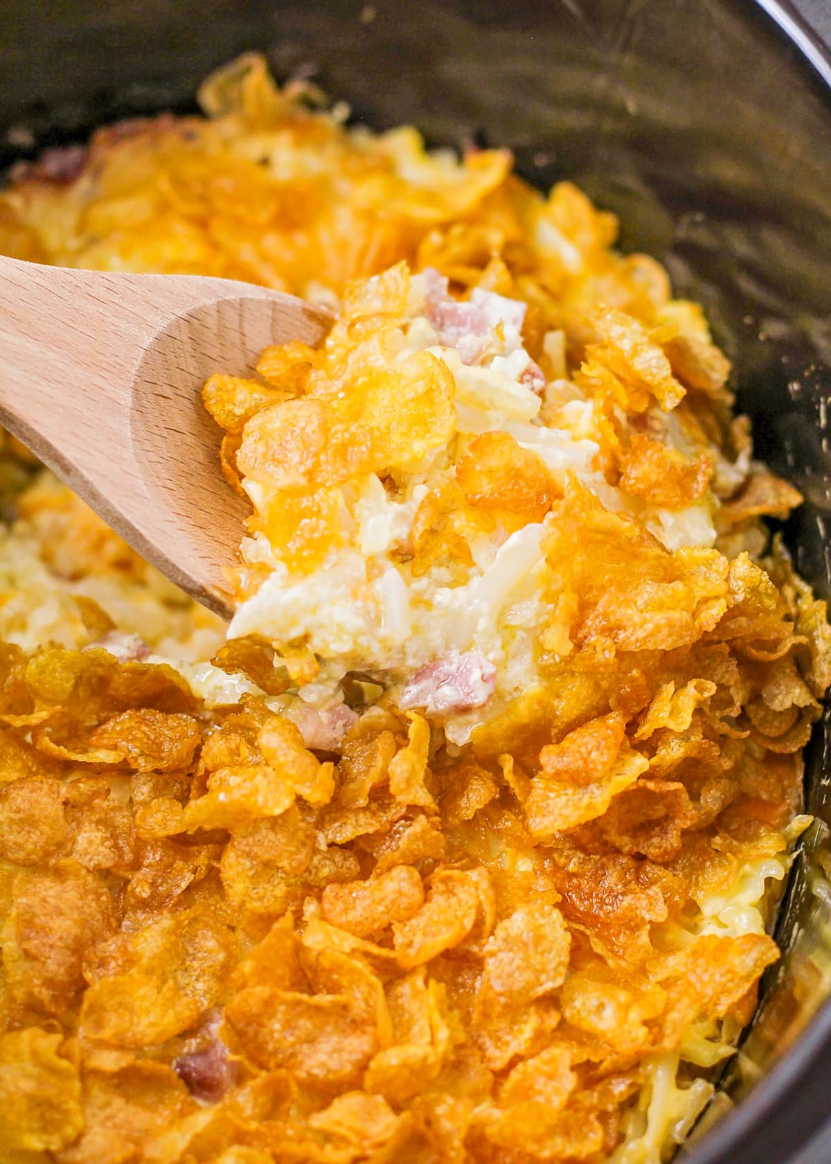 Scooping crockpot hashbrown casserole from a slow cooker.