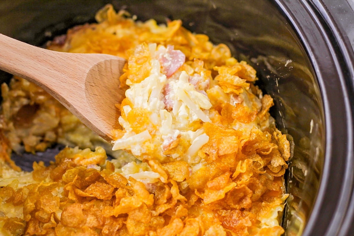 Crockpot hashbrown casserole being scooped from a slow cooker.